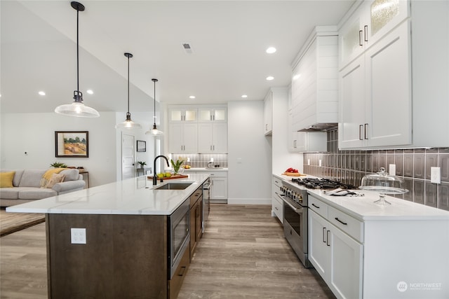 kitchen with light stone countertops, appliances with stainless steel finishes, a kitchen island with sink, pendant lighting, and white cabinetry