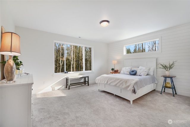 bedroom featuring multiple windows, light carpet, and wood walls