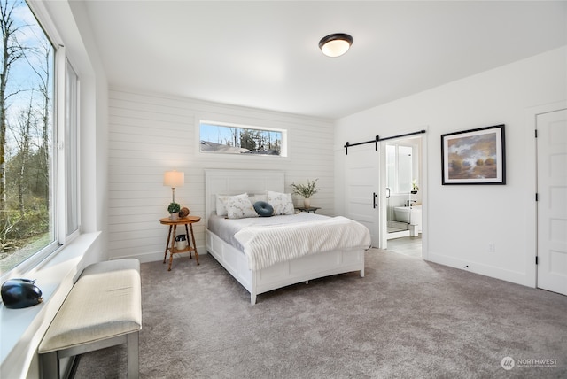 bedroom featuring a barn door, carpet floors, wooden walls, and connected bathroom