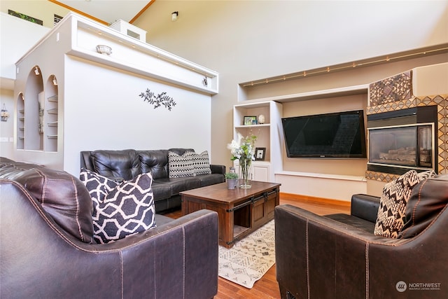 living room featuring a high ceiling, hardwood / wood-style floors, a tile fireplace, and built in shelves