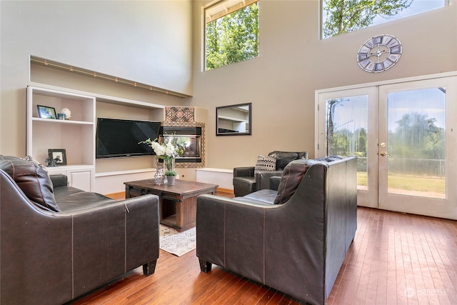 living room featuring french doors, light hardwood / wood-style floors, a healthy amount of sunlight, and a towering ceiling