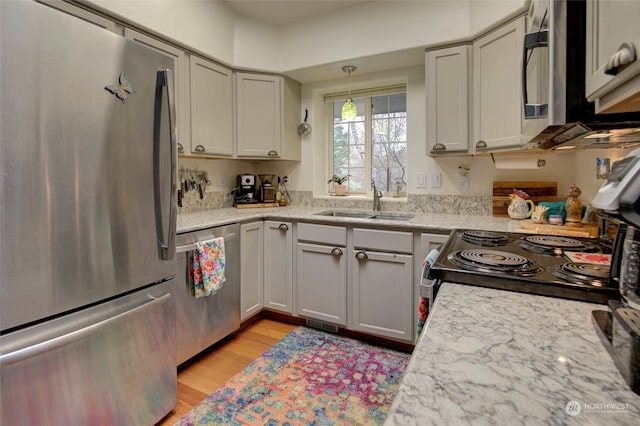 kitchen with light stone countertops, hanging light fixtures, appliances with stainless steel finishes, light hardwood / wood-style floors, and sink