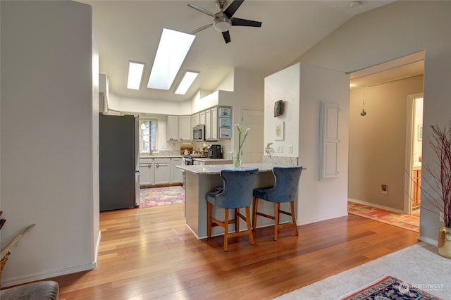 kitchen featuring kitchen peninsula, ceiling fan, a breakfast bar, light hardwood / wood-style flooring, and stainless steel appliances