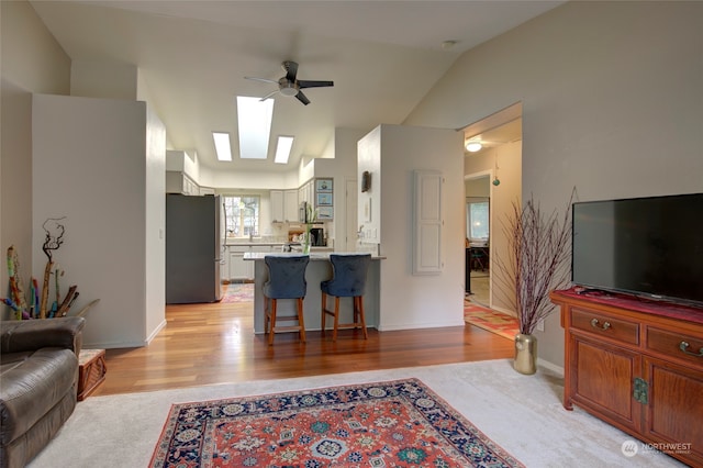 living room featuring lofted ceiling with skylight, light hardwood / wood-style floors, and ceiling fan