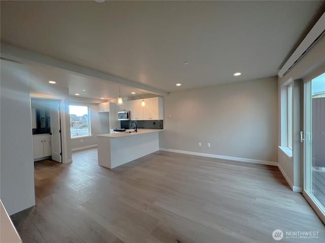 kitchen with white cabinets, light wood-style flooring, a peninsula, hanging light fixtures, and light countertops