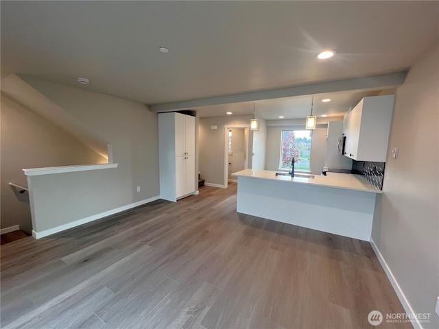 kitchen featuring white cabinets, decorative light fixtures, a peninsula, light countertops, and a sink