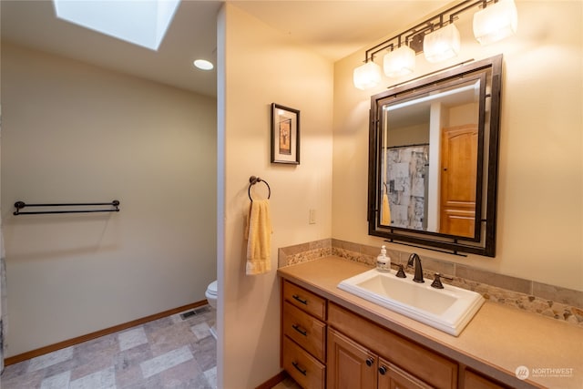 bathroom featuring toilet, vanity with extensive cabinet space, tile floors, and a skylight