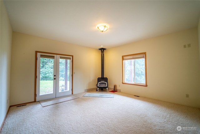 carpeted empty room with a wood stove, a wealth of natural light, and french doors