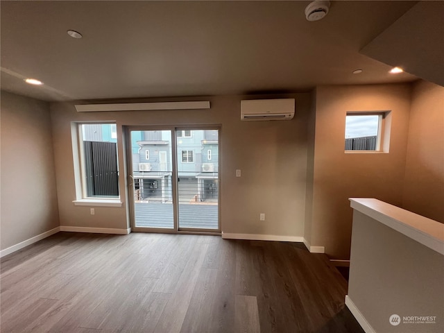 spare room featuring a wall mounted AC, plenty of natural light, and wood-type flooring