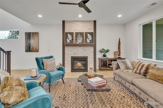 living room with light hardwood / wood-style floors, a stone fireplace, and ceiling fan