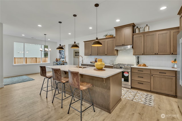 kitchen featuring a kitchen bar, light wood-type flooring, stainless steel gas range oven, decorative light fixtures, and a center island with sink