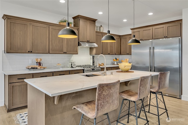 kitchen with high quality fridge, a breakfast bar, pendant lighting, light hardwood / wood-style floors, and an island with sink