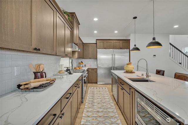 kitchen with pendant lighting, sink, built in appliances, light wood-type flooring, and a breakfast bar area