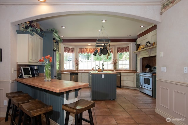 kitchen featuring kitchen peninsula, white cabinetry, a kitchen bar, stainless steel appliances, and crown molding