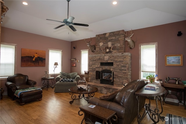 living room with light hardwood / wood-style floors, ceiling fan, and a stone fireplace