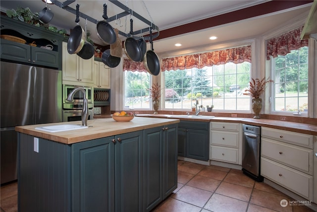 kitchen with stainless steel appliances, light tile flooring, a center island with sink, butcher block counters, and sink