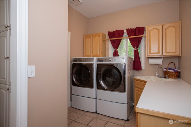 clothes washing area featuring sink, cabinets, light tile floors, and washer and clothes dryer