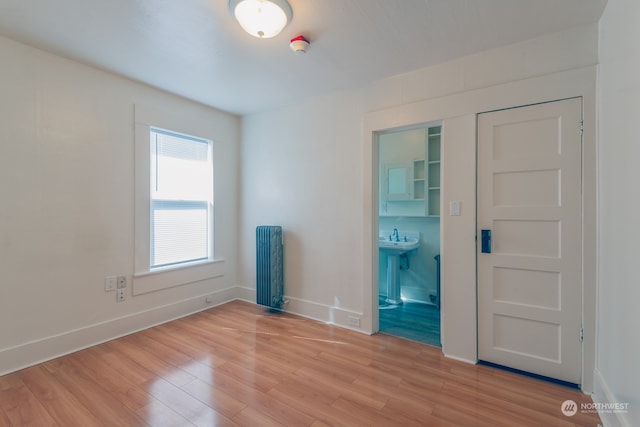 unfurnished room featuring light hardwood / wood-style floors, sink, and radiator heating unit