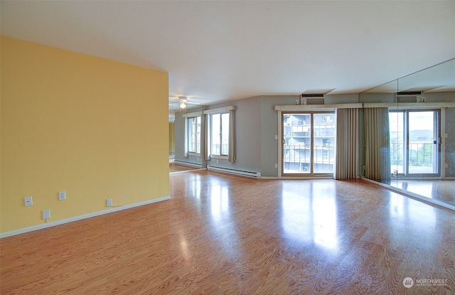 unfurnished room with ceiling fan, a wealth of natural light, a baseboard heating unit, and light hardwood / wood-style floors