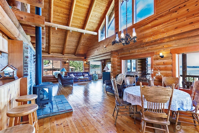 dining area with rustic walls, beam ceiling, wood-type flooring, wooden ceiling, and a wood stove