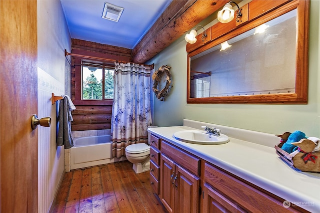 full bathroom with shower / tub combo with curtain, hardwood / wood-style flooring, rustic walls, vanity, and toilet