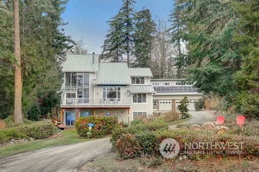 view of front facade featuring dirt driveway, a standing seam roof, metal roof, a balcony, and a garage