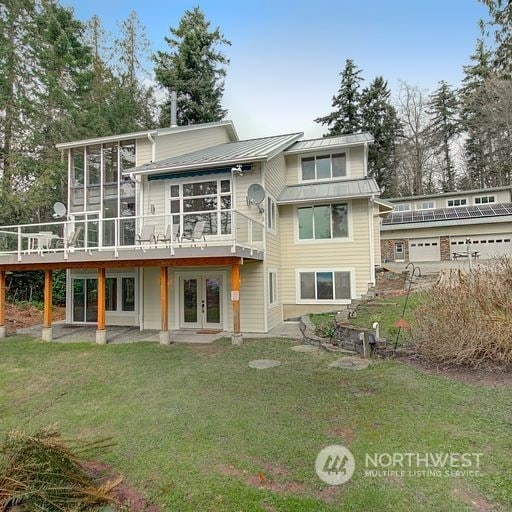 back of property featuring a garage, a wooden deck, french doors, and a lawn