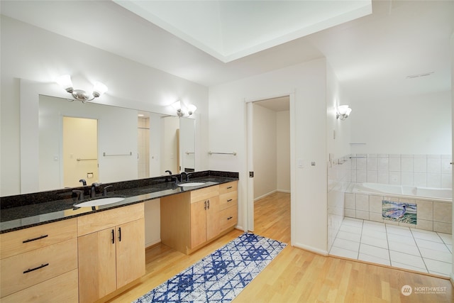 bathroom with hardwood / wood-style floors, tiled bath, and vanity