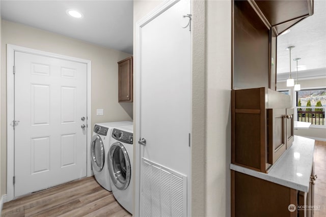 laundry area featuring separate washer and dryer, light hardwood / wood-style flooring, and cabinets