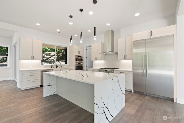 kitchen featuring stainless steel appliances, hanging light fixtures, a kitchen island, hardwood / wood-style flooring, and wall chimney exhaust hood