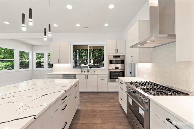 kitchen with hanging light fixtures, decorative backsplash, wall chimney exhaust hood, appliances with stainless steel finishes, and dark wood-type flooring