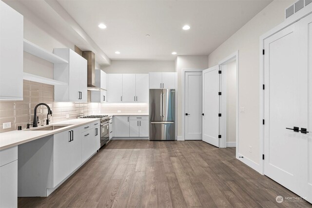 kitchen featuring appliances with stainless steel finishes, tasteful backsplash, hardwood / wood-style floors, and wall chimney exhaust hood