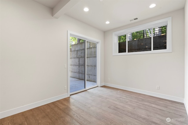 spare room with beam ceiling and light wood-type flooring