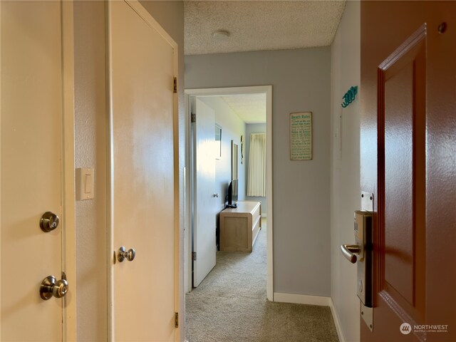 corridor featuring a textured ceiling and light colored carpet