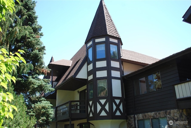 view of side of home with stone siding, roof with shingles, and stucco siding