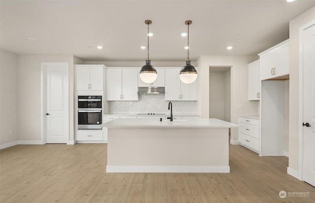 kitchen with a kitchen island with sink, white cabinets, decorative light fixtures, and stainless steel double oven