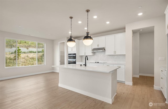 kitchen with white cabinetry, tasteful backsplash, a center island with sink, pendant lighting, and black appliances