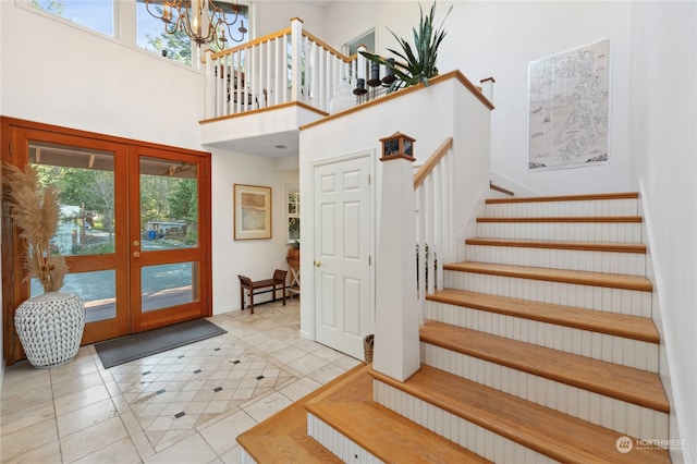 interior space with a high ceiling, a notable chandelier, french doors, and light tile flooring