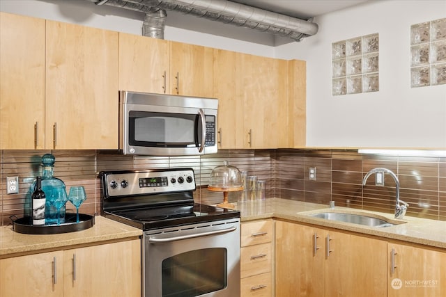 kitchen featuring appliances with stainless steel finishes, backsplash, light brown cabinetry, light stone counters, and sink