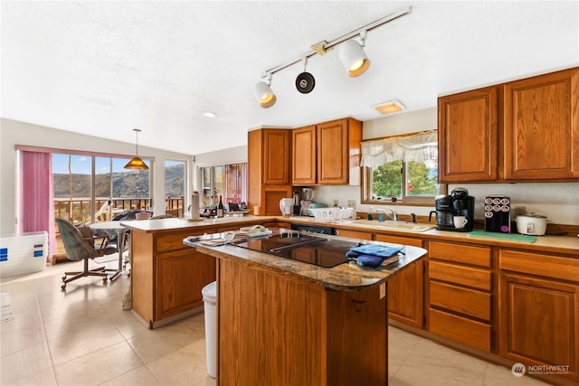 kitchen featuring a peninsula, a kitchen island, a sink, brown cabinetry, and pendant lighting