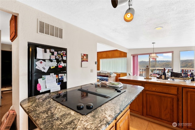 kitchen with a textured ceiling, visible vents, hanging light fixtures, brown cabinets, and black appliances