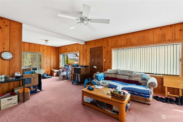 carpeted living area with beamed ceiling, wooden walls, and ceiling fan