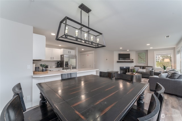 dining room featuring a large fireplace, sink, a chandelier, and light wood-type flooring