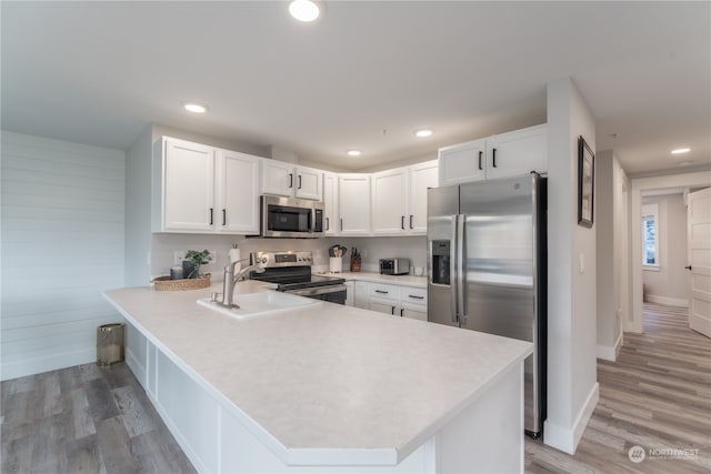 kitchen with stainless steel appliances, light wood-type flooring, white cabinetry, and kitchen peninsula