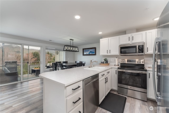 kitchen featuring sink, hanging light fixtures, light hardwood / wood-style floors, stainless steel appliances, and white cabinetry