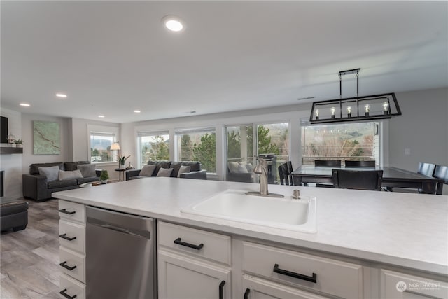 kitchen featuring stainless steel dishwasher, light hardwood / wood-style floors, white cabinetry, hanging light fixtures, and sink