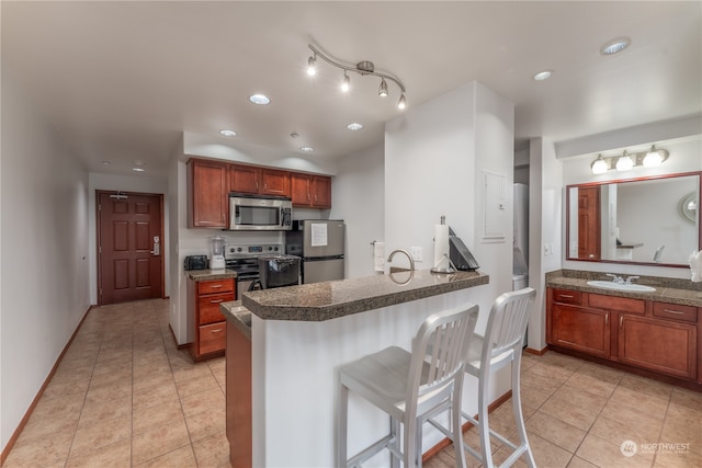 kitchen featuring appliances with stainless steel finishes, a breakfast bar area, light tile floors, track lighting, and sink