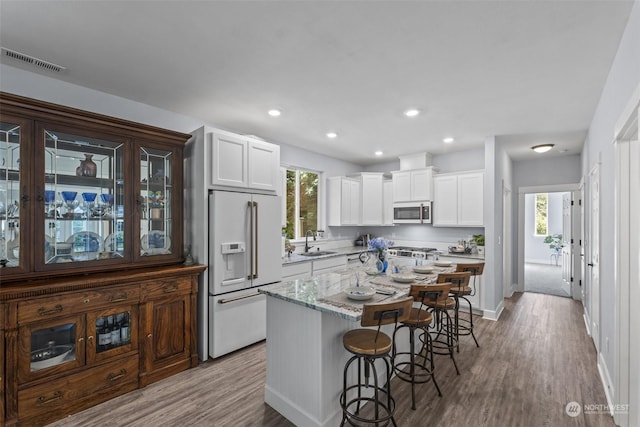 kitchen featuring a breakfast bar, a center island, sink, high end fridge, and white cabinetry