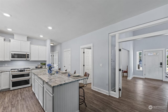 kitchen with light stone countertops, a center island, range with two ovens, a breakfast bar area, and white cabinets