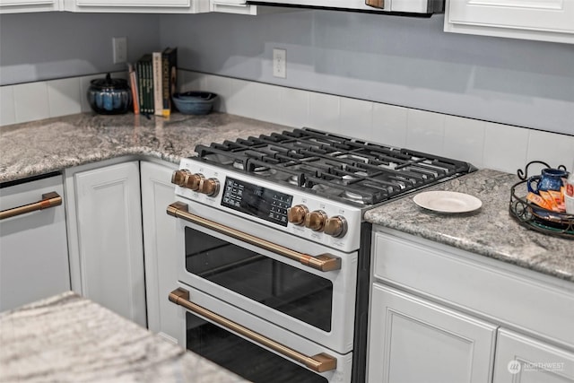 kitchen with white cabinets, light stone counters, stainless steel stove, and tasteful backsplash